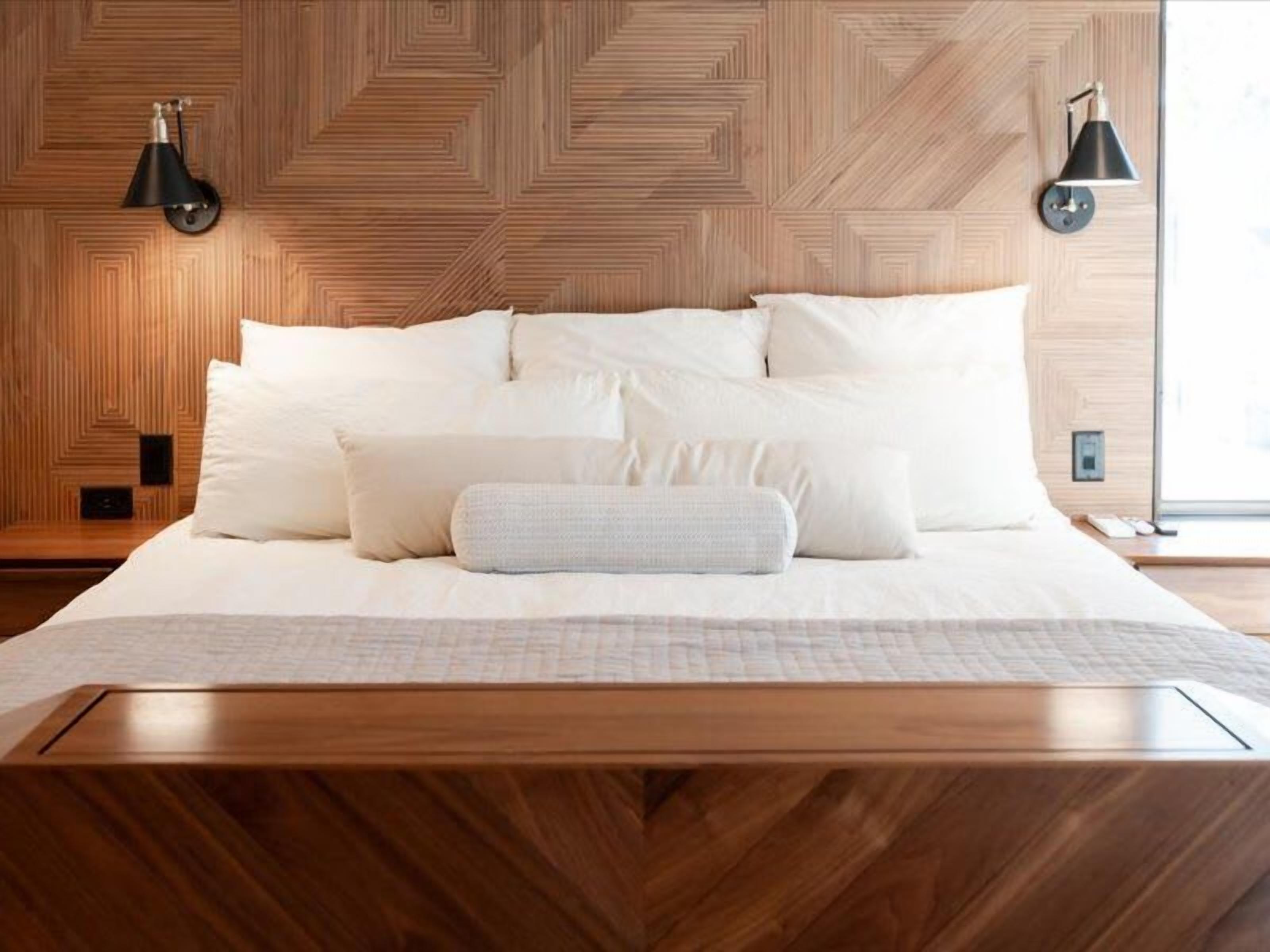 A bed with white bedding, two bedside lamps, and a wooden headboard with a geometric pattern.