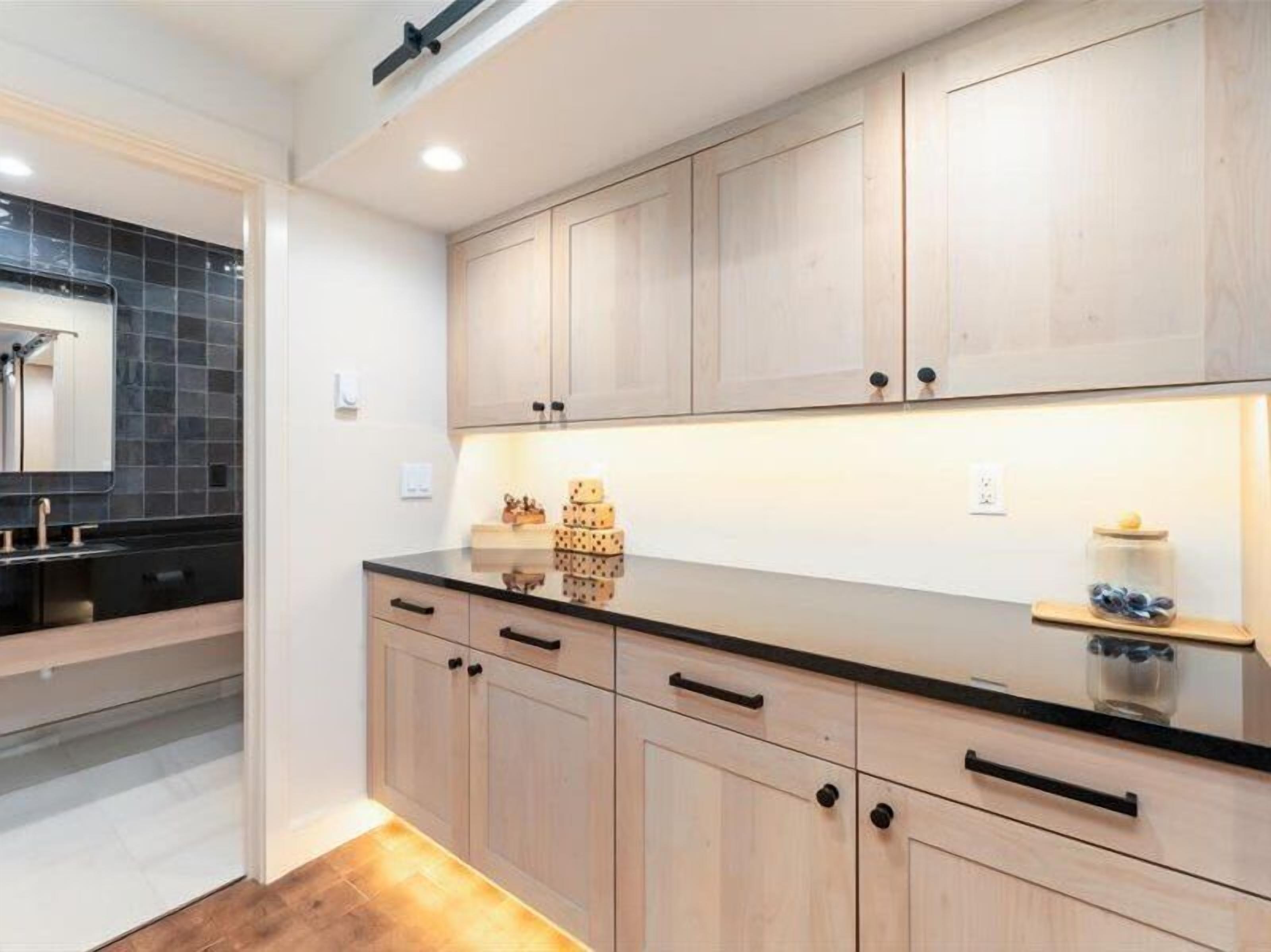 A modern kitchen with light wood cabinets, a black countertop, and a built-in oven.