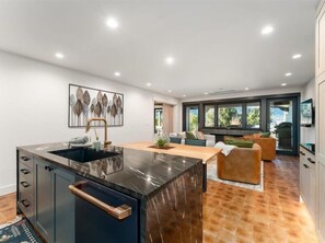 A modern kitchen with a central island, a dining area with a sofa, and a large window providing a view of the outdoors. - Luxury Condo E1 + Hot tub at Wapato Point Chelan (Manson)