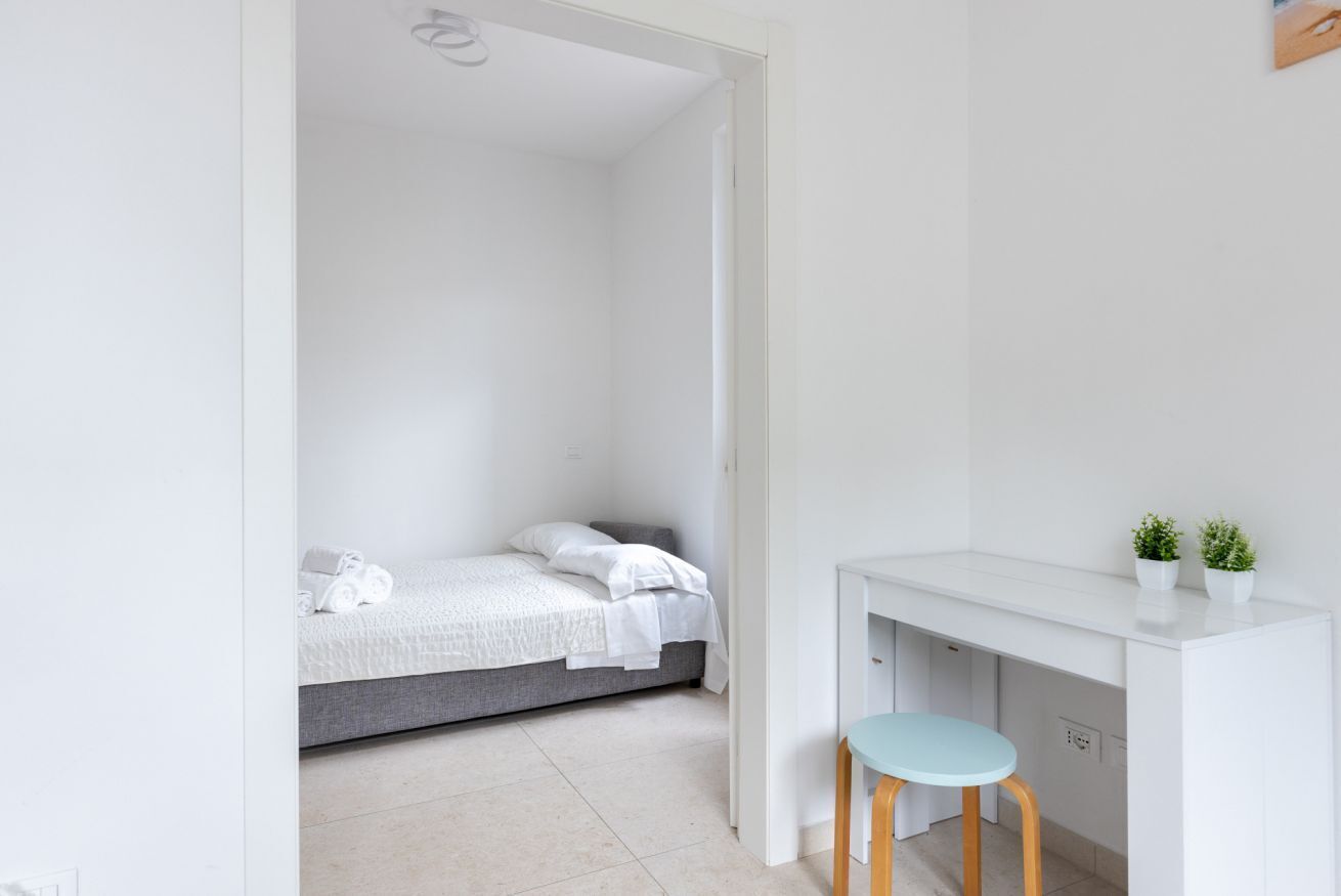 A minimalist room with a bed, a desk, and two potted plants.