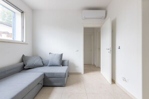 Ein modernes Wohnzimmer mit einem grauen Ecksofa, einem Fenster und einem Gang zu einem anderen Raum.