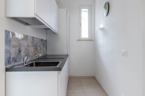 Eine Küche mit integriertem Spülbecken, weißen Schränken, einem Fenster und einer Marmor-Spritzschutzwand.