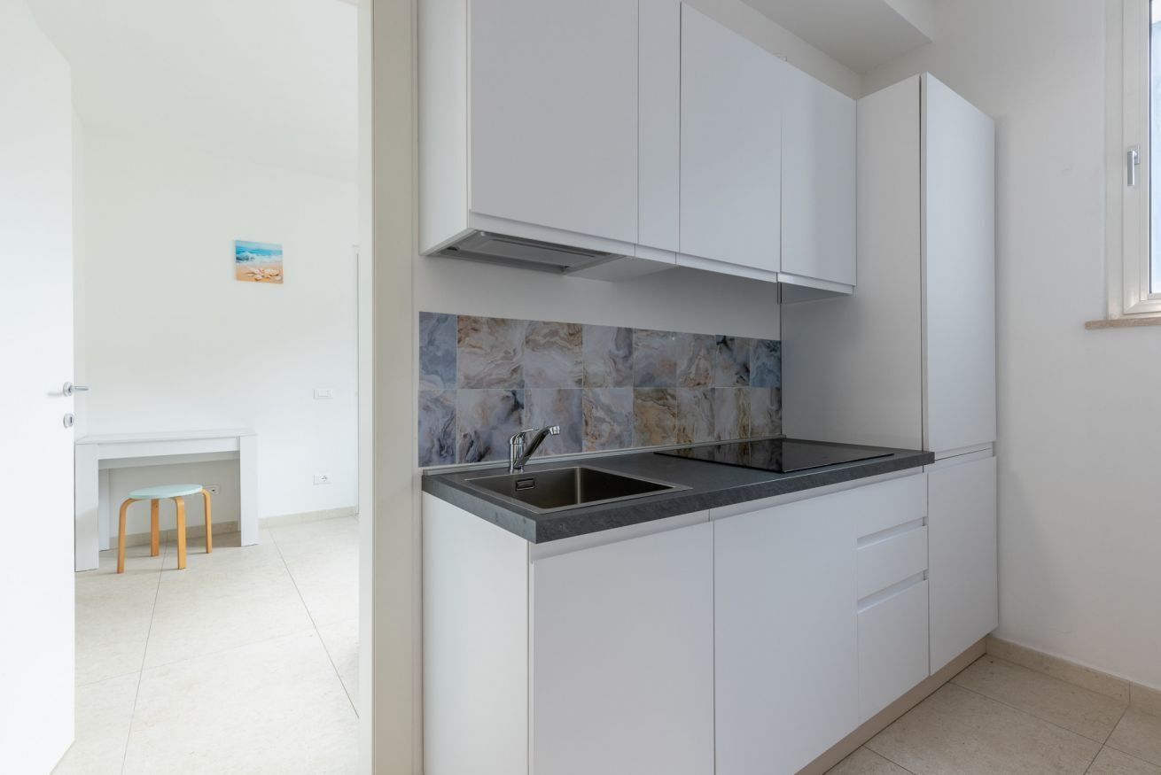 Een moderne keuken met witte kastjes, een marmeren spatwand en een zwart aanrecht.