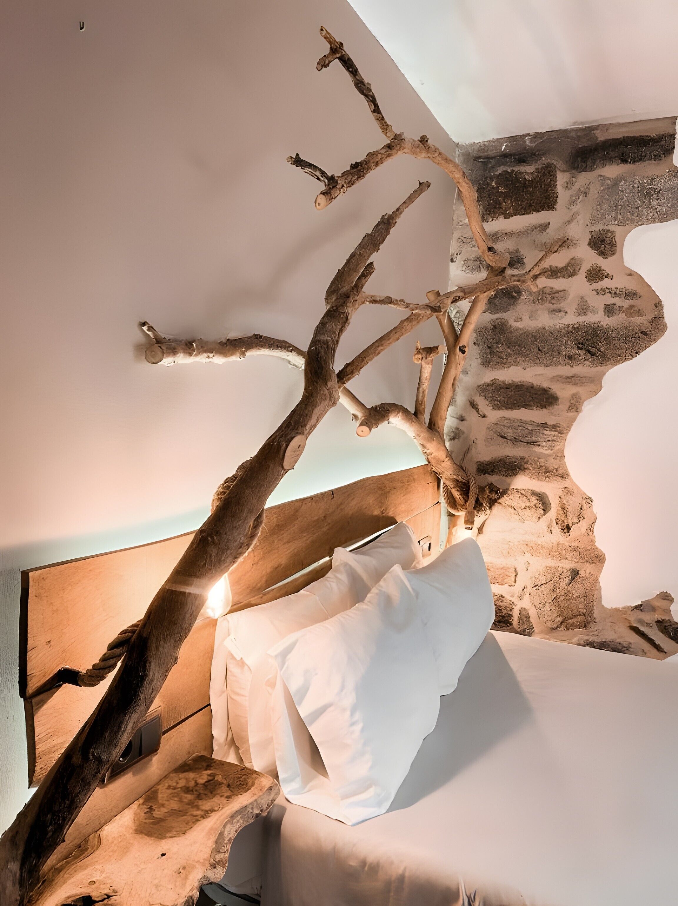 Una habitación con una cama, una pared de piedra y una estructura de ramas.