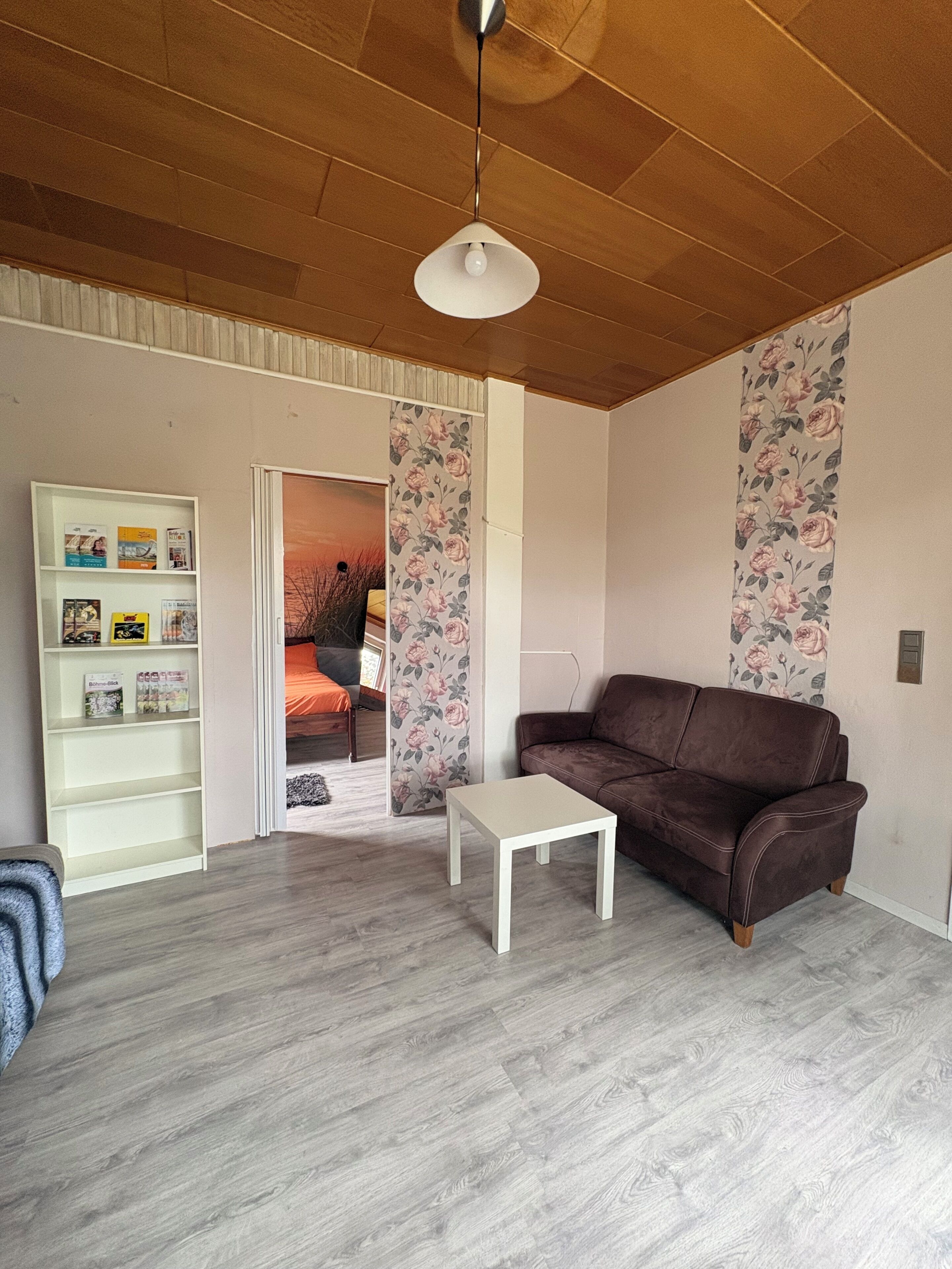 A living room with a brown leather sofa, a white coffee table, a bookshelf, and a door leading to another room.
