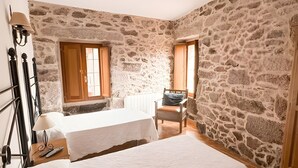 A bedroom with a stone wall, a bed, a chair, and a window. - Double Diamond Room with 2 Beds, Interior Patio, and Wi-Fi (Porqueirós)