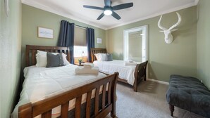 A bedroom with two beds, a ceiling fan, a mounted deer head, and a window with curtains. - 201-4thStreet-207 (Austin)