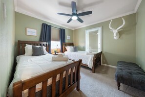 A bedroom with two beds, a ceiling fan, a mounted deer head, and a window with curtains. - 201-4thStreet-207 (Austin)
