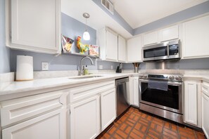 A modern kitchen with white cabinetry, a stainless steel microwave, an oven, and a dishwasher. - 201-4thStreet-207 (Austin)