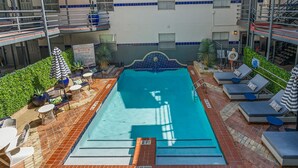 A rooftop pool with lounge chairs and umbrellas, surrounded by a brick patio and a building with blue-tiled windows. - 201-4thStreet-207 (Austin)
