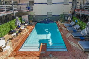 A rooftop pool with lounge chairs and umbrellas, surrounded by a brick patio and a building with blue-tiled windows. - 201-4thStreet-207 (Austin)