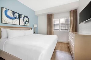 Habitación de hotel con una cama grande, un televisor de pantalla plana, una ventana con cortinas y arte abstracto en la pared.