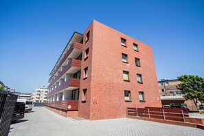 A multi-story brick building with balconies, a paved ground floor, and a clear blue sky. - Vrbo Property (Westerland)