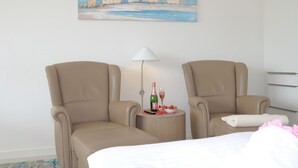 Une chambre d’hôtel avec deux fauteuils en cuir, un lit, une petite table avec une bouteille et des verres, et un tableau au mur.