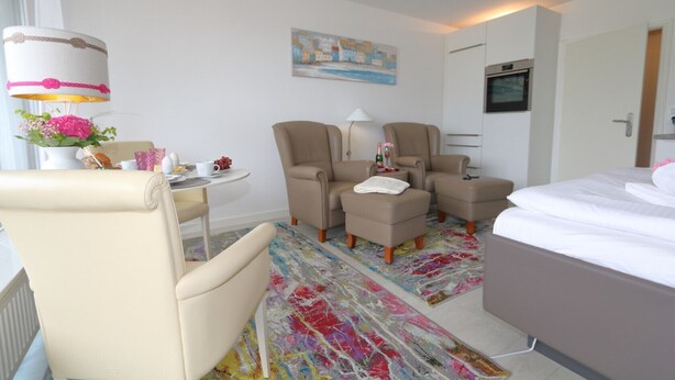 Une chambre d’hôtel avec un lit, deux fauteuils, une petite table avec une lampe, un tableau au mur et un tapis coloré.