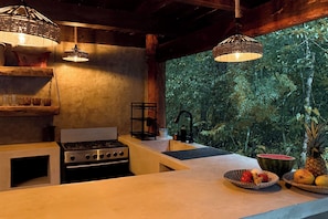 Una cocina con estufa a gas, lámparas colgantes y vista a la vegetación densa.