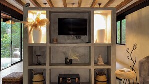 Una sala de estar moderna con una televisión, estanterías con adornos, un sillón de mimbre y un ventanal grande.