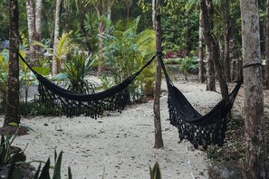 A hammock suspended between trees in a forested area with sandy ground.