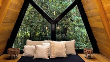 Um quarto aconchegante com cama, almofadas e vista para uma floresta por uma grande janela.