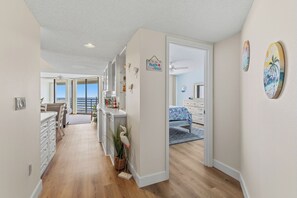 A hallway with a view to a balcony, a dining area with a table and chairs, and a bedroom with a bed and a window. - 🏊🥽🌴Ebb Tide 406 | NSB's Finest | New Pool + Sundeck + Beach Access (New Smyrna Beach)