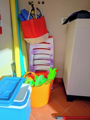 Ein Raum mit einer blauen Aufbewahrungsbox, einem gelben Eimer mit grünen Gegenständen, einer roten Tasche und einem weißen Gerät.