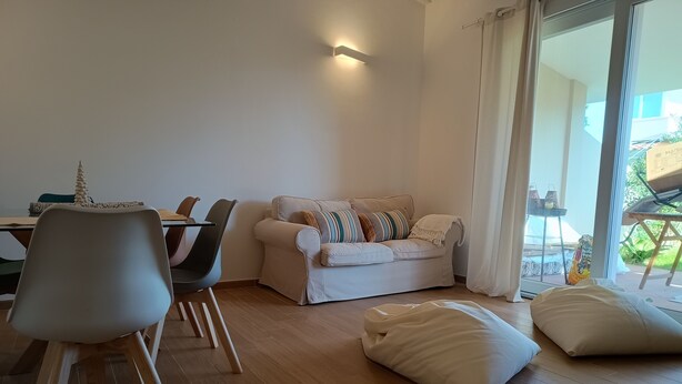 En moderne stue med sofa, spisebord, stole og et stort vindue.