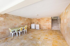 Ein Zimmer mit Fliesenboden, einem Tisch mit Stühlen, einem kleinen weißen Schrank und einer Treppe, die in ein Obergeschoss führt.