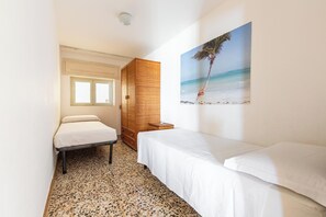 A small, narrow hotel room with a bed, a wooden wardrobe, a small table, and a painting of a beach scene. - Dimora Mina by BarbarHouse (Patù)