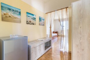 A room with a bed, a small table, a refrigerator, and a window with curtains. - Dimora Mina by BarbarHouse (Patù)