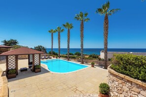 Ein Poolbereich mit freiem Blick auf das Meer, umgeben von Palmen und einem Pavillon.