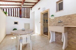 A small, enclosed patio with a round table and chairs, a built-in sink, and a wooden ceiling structure. - Dimora Mina by BarbarHouse (Patù)