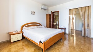 Une chambre à coucher avec un lit en bois, une table de chevet, une armoire et une salle de bain visible à travers une porte ouverte.