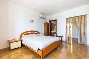 Ein Schlafzimmer mit einem hölzernen Bett, einem Nachttisch, einem Kleiderschrank und einem durch eine geöffnete Tür einsehbaren Badezimmer.