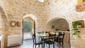 A stone-walled room with a dining table, chairs, and a kitchen area. - Trullo Sobba Llera by BarbarHouse (San Michele Salentino)