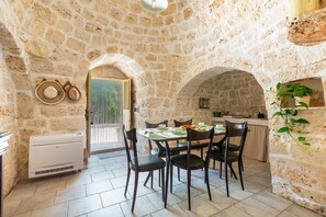 Una habitación con paredes de piedra, una mesa de comedor, sillas y una zona de cocina.