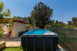 Una piscina con valla de seguridad, un área de patio con sillas y un muro de piedra.