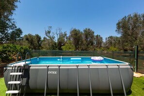 Una piscina inflable con escalera, rodeada por una valla y árboles al fondo.