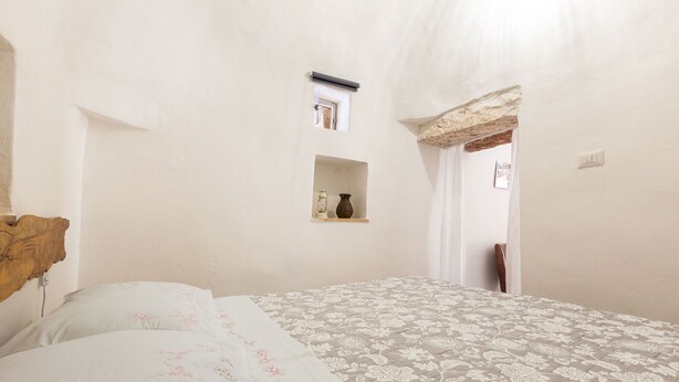A bedroom with a bed, a small shelf with a vase, and a window. - Trullo Sobba Llera by BarbarHouse (San Michele Salentino)