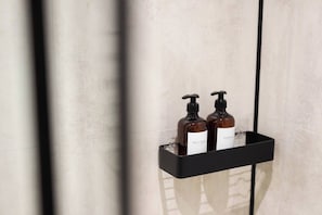 A bathroom with a black soap dispenser shelf holding two bottles of body wash and shampoo.
