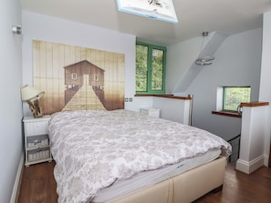 A bedroom with a bed, a nightstand, a lamp, a wall-mounted shelf, a window with blinds, and a staircase. - 5 Hall Yard (Whitby)