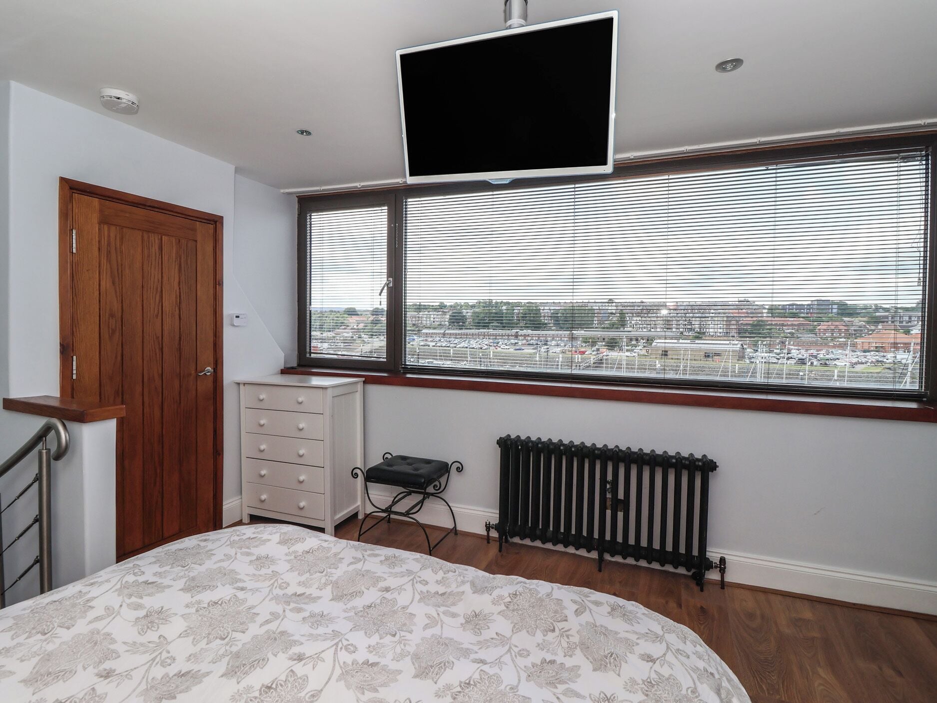 A bedroom with a bed, a dresser, a radiator, a TV, a window with blinds, and a door.