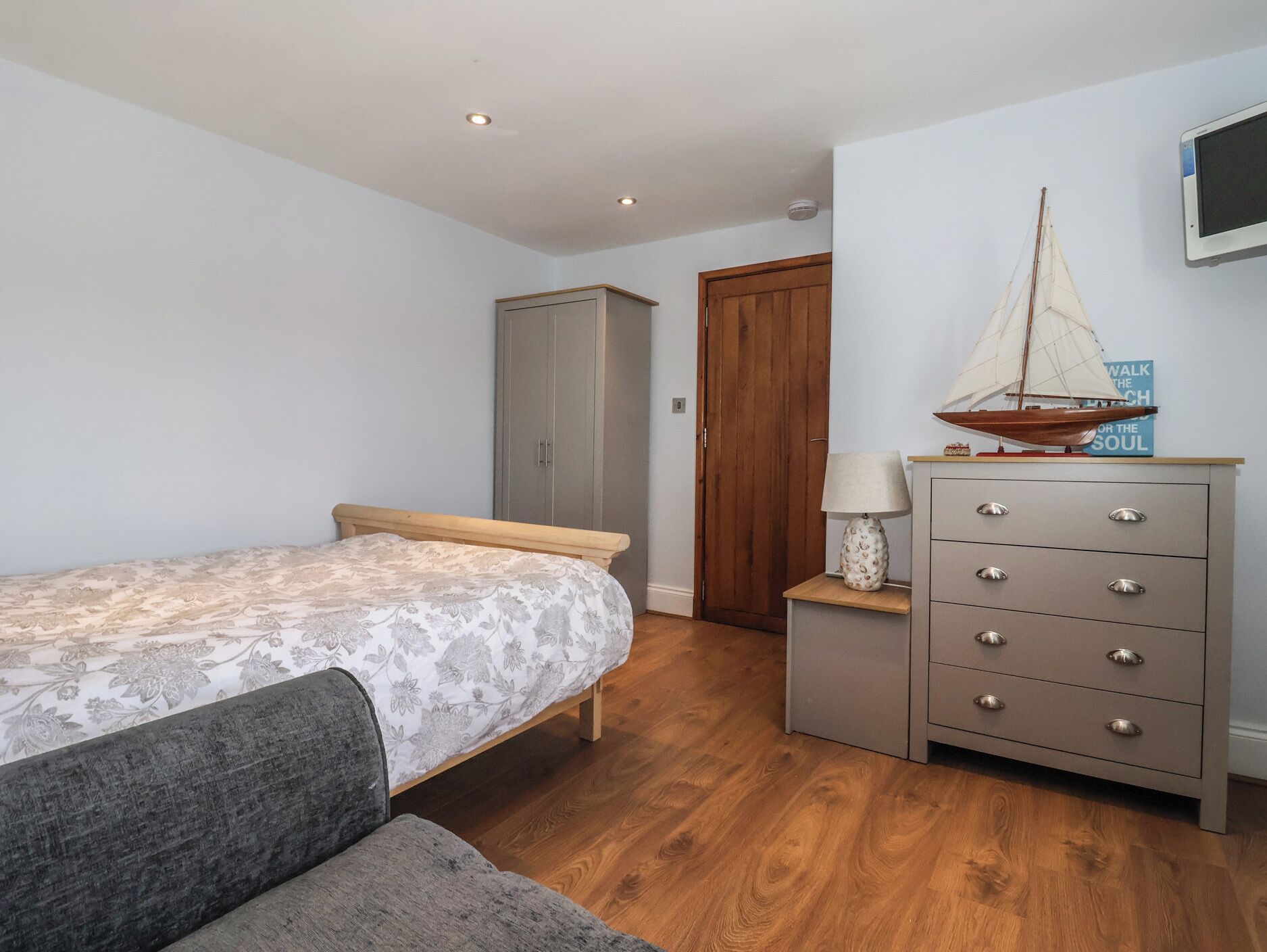 A bedroom with a bed, a dresser, a wooden wardrobe, a lamp, and a sailboat model.