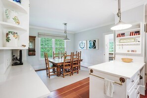 A kitchen with a dining table, chairs, and a white island with a sink. - Shelter Island Estate · Heated Pool · Guest Cottage · Walk to Beach · Sleeps 10 (Shelter Island Heights)