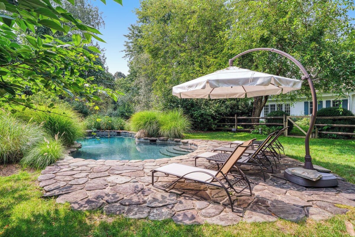 A backyard with a stone patio, a pool, and a swing chair under a canopy.