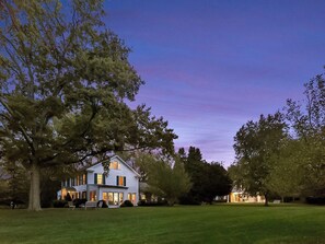 A large two-story house with a well-maintained lawn and trees in the foreground. - Shelter Island Estate · Heated Pool · Guest Cottage · Walk to Beach · Sleeps 10 (Shelter Island Heights)