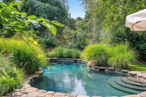 A swimming pool surrounded by lush greenery and stone steps leading into the water. - Shelter Island Estate · Heated Pool · Guest Cottage · Walk to Beach · Sleeps 10 (Shelter Island Heights)