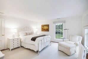 A bedroom with a bed, bedside tables, a chair, and a window. - Shelter Island Estate · Heated Pool · Guest Cottage · Walk to Beach · Sleeps 10 (Shelter Island Heights)
