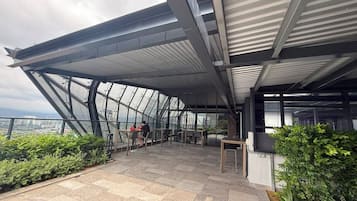 Una terraza moderna en la azotea con techo de vidrio, mobiliario exterior y vistas de la ciudad.