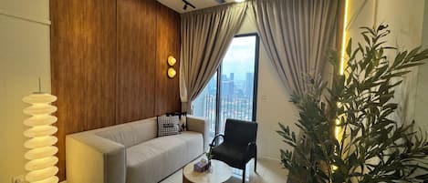 A modern living room with a sofa, a coffee table, a chair, a ceiling fan, and a large window with curtains.