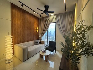 Un salon moderne comprenant un canapé, une table basse, un fauteuil, un ventilateur de plafond et une grande fenêtre avec des rideaux.